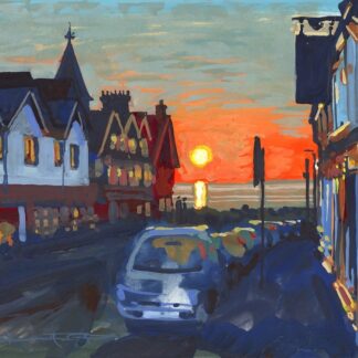 sunset over the sea viewed down a street with cars parked on the right and a hotel at the end