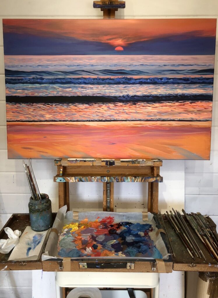 painting of a colourful sunset over the sea on an easel in an artist's studio