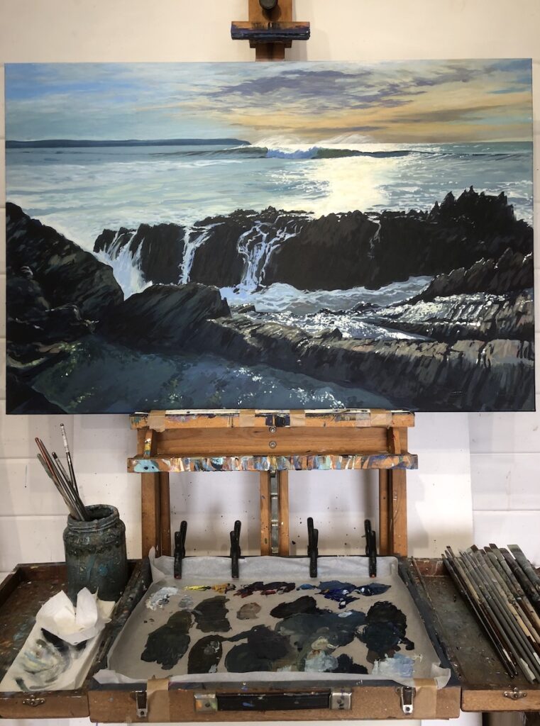 painting of breaking waves on a rocky shore on an artist's easel