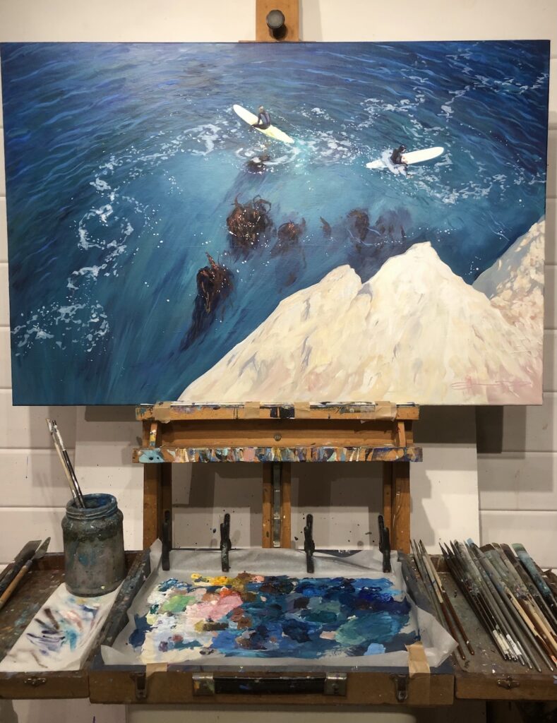 painting of two surfers sat on their surfboards in the ocean on an artist's easel