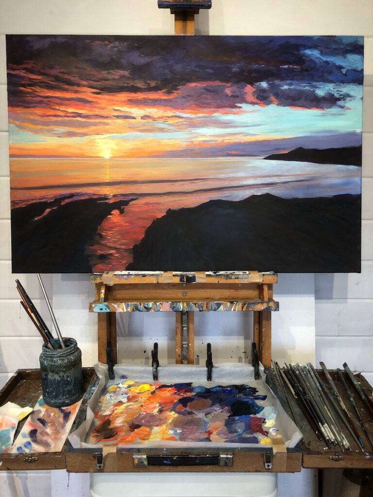 golden sunset and ocean waves painting on an easel in an artist's studio